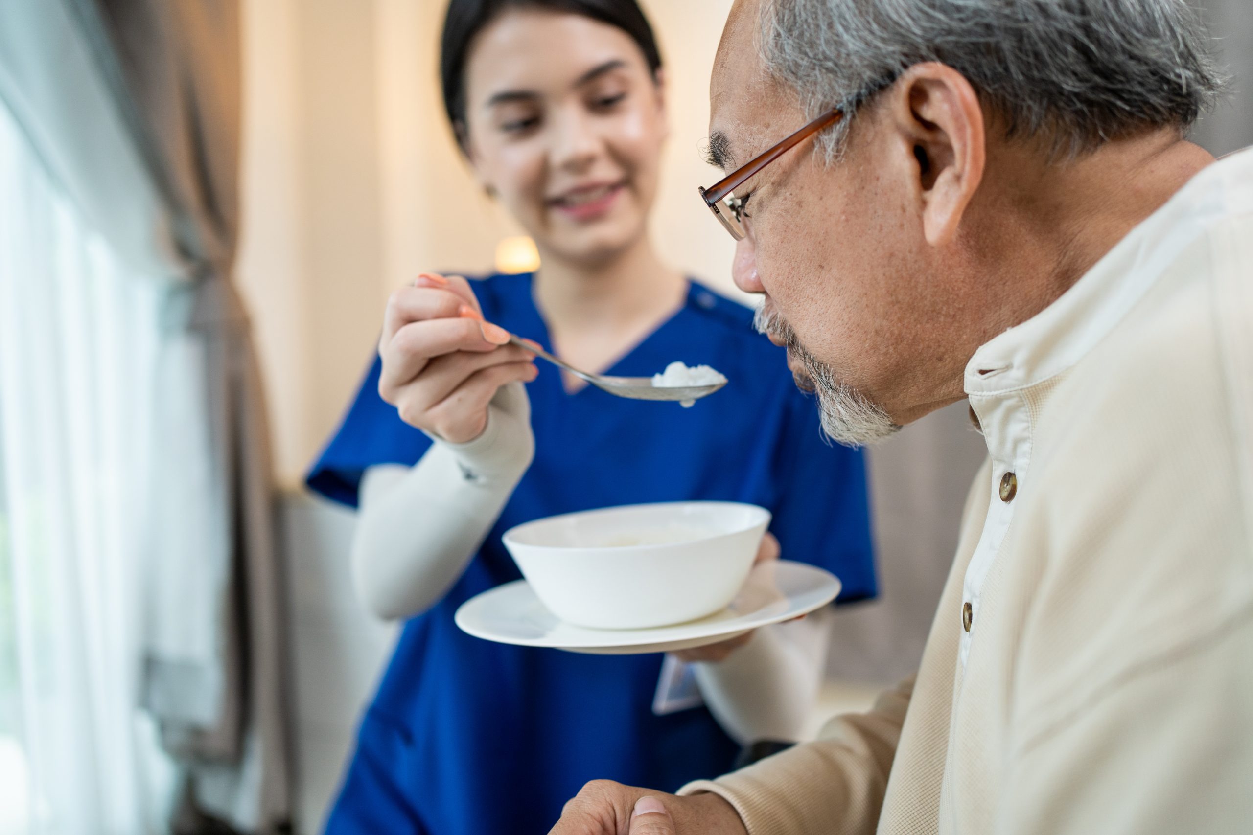 Asian beautiful therapist doctor serve food to older patient in house.